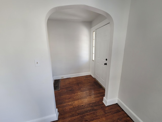 hall featuring baseboards, visible vents, arched walkways, and dark wood-style flooring