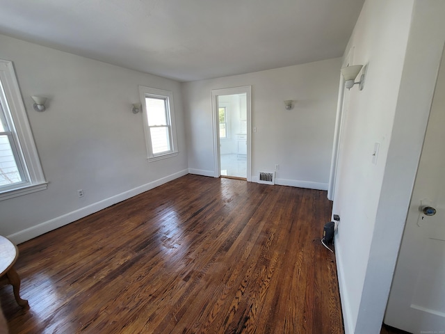 spare room featuring baseboards, visible vents, and dark wood-style flooring