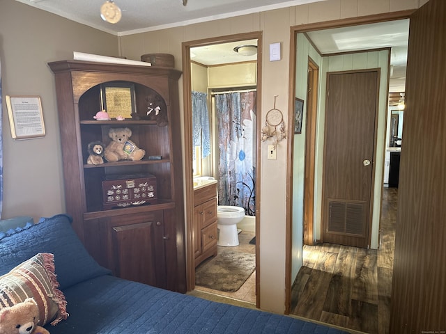 bedroom featuring connected bathroom, visible vents, crown molding, and wood finished floors