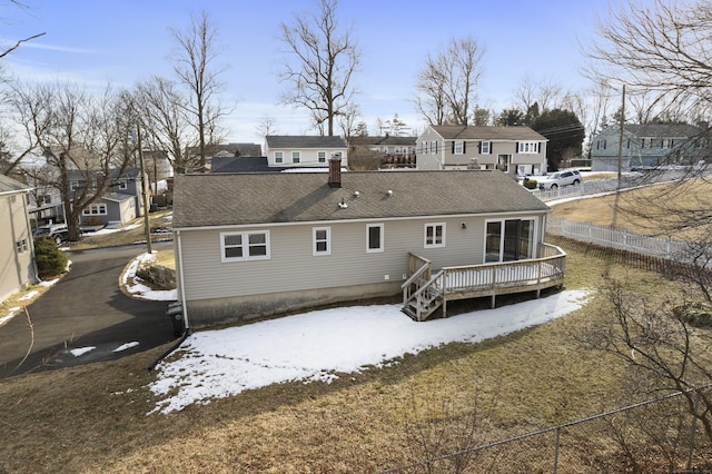 snow covered back of property featuring a shingled roof, a residential view, fence, and a deck