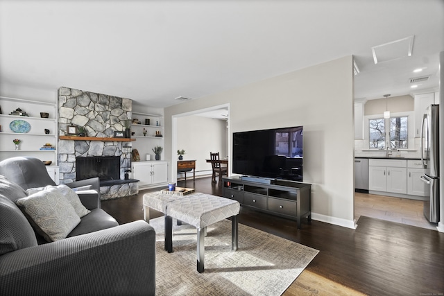 living room featuring baseboards, visible vents, wood finished floors, baseboard heating, and a stone fireplace