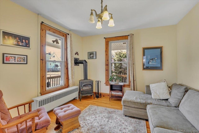 living room featuring radiator, a wood stove, an inviting chandelier, and wood finished floors