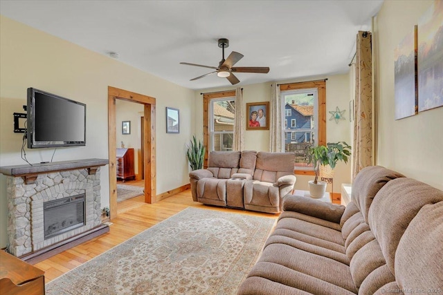 living room with baseboards, a stone fireplace, a ceiling fan, and light wood-style floors