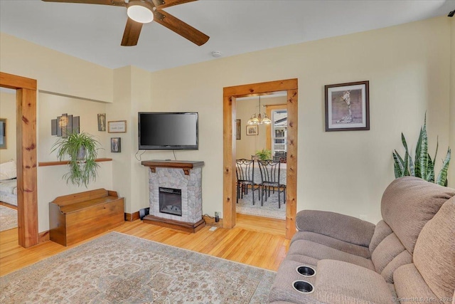 living area featuring a fireplace, wood finished floors, baseboards, and a ceiling fan