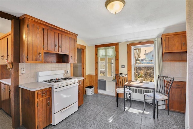 kitchen featuring tasteful backsplash, a wainscoted wall, light countertops, white gas range, and granite finish floor