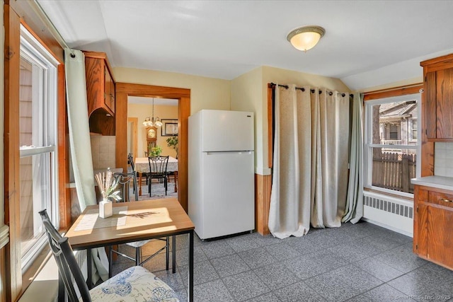 kitchen with brown cabinets, radiator heating unit, freestanding refrigerator, baseboards, and a chandelier