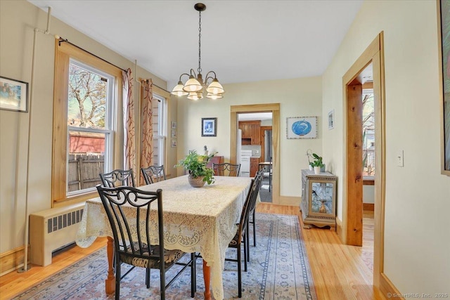 dining room featuring a notable chandelier, baseboards, radiator, and light wood-style flooring