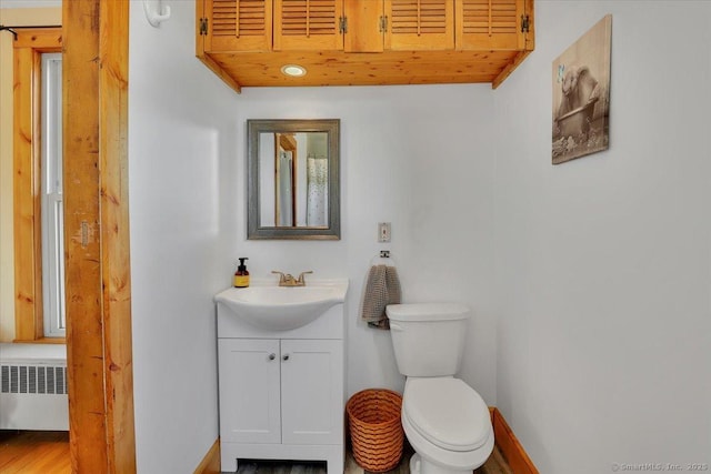 half bathroom with vanity, radiator, toilet, and baseboards