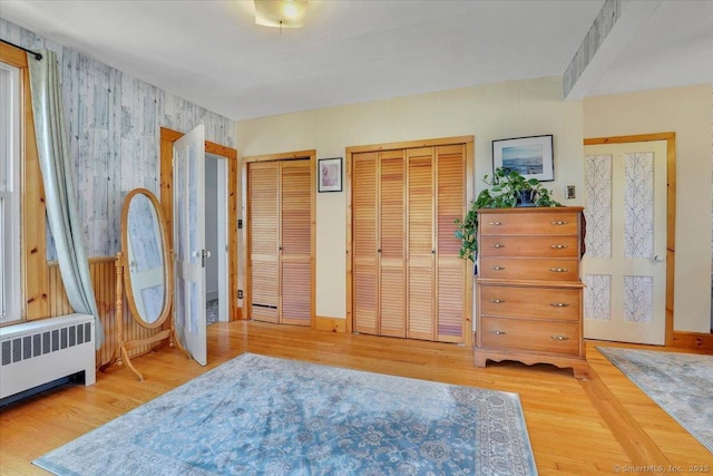 bedroom with two closets, wood finished floors, and radiator heating unit