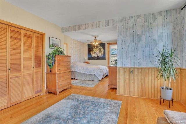 bedroom with wallpapered walls, wood finished floors, a closet, and wainscoting