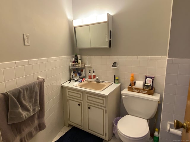 bathroom featuring a wainscoted wall, tile walls, toilet, vanity, and tile patterned flooring