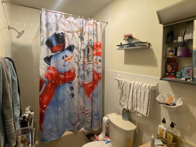 full bath with toilet, shower / tub combo with curtain, tile walls, and wainscoting