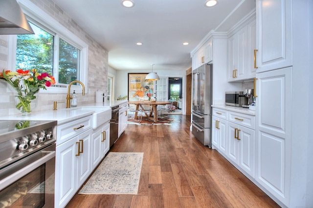 kitchen featuring a sink, white cabinetry, high end appliances, dark wood finished floors, and decorative light fixtures