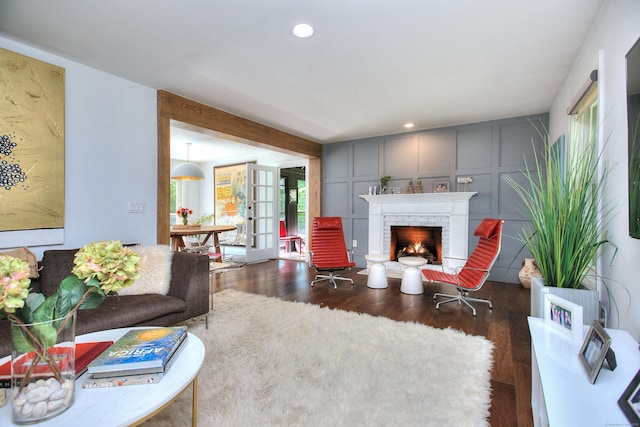 living room featuring a decorative wall, recessed lighting, french doors, a brick fireplace, and dark wood finished floors