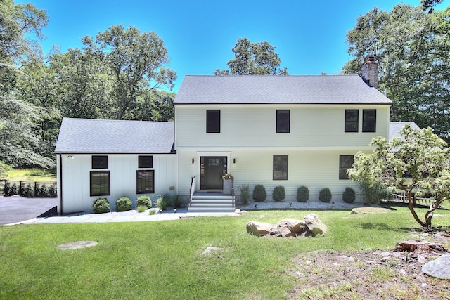 view of front of house with a shingled roof, a chimney, a front yard, and board and batten siding