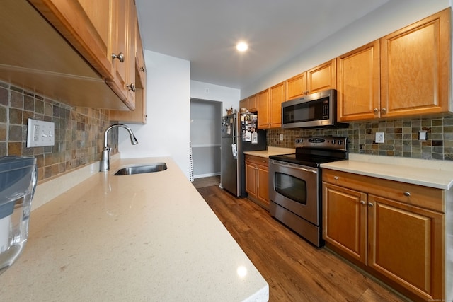 kitchen featuring stainless steel appliances, a sink, backsplash, dark wood-style floors, and brown cabinetry