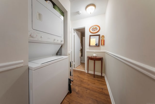 clothes washing area featuring stacked washing maching and dryer, baseboards, laundry area, and wood finished floors