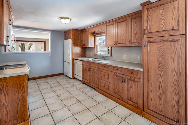 kitchen featuring white appliances, a sink, baseboards, light countertops, and brown cabinets