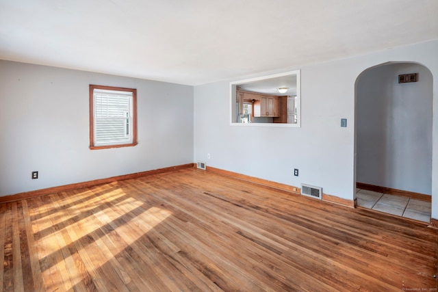 empty room featuring arched walkways, wood finished floors, visible vents, and baseboards