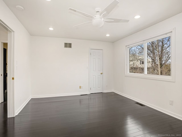 empty room featuring dark wood-style flooring, visible vents, and baseboards