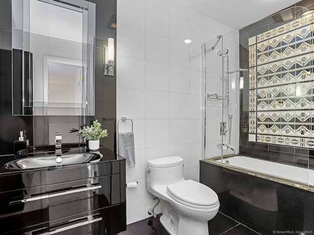 bathroom with vanity, tile walls, toilet, and bath / shower combo with glass door