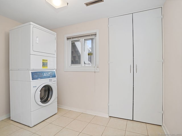 clothes washing area featuring light tile patterned floors, laundry area, visible vents, baseboards, and stacked washer / drying machine