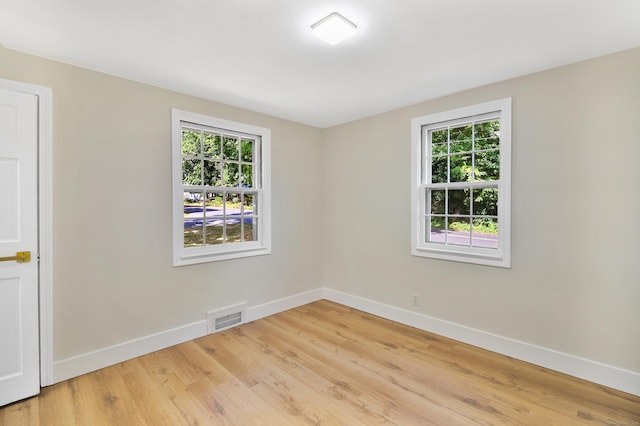 spare room featuring light wood finished floors, plenty of natural light, visible vents, and baseboards