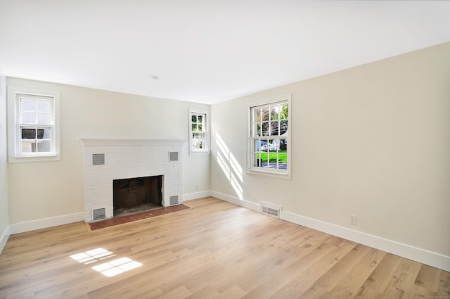 unfurnished living room featuring baseboards, visible vents, a fireplace, and light wood finished floors