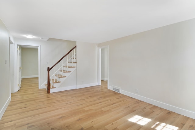 unfurnished room featuring light wood-style flooring, visible vents, stairway, and baseboards