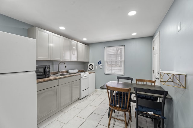 kitchen featuring white appliances, baseboards, white cabinets, a sink, and recessed lighting