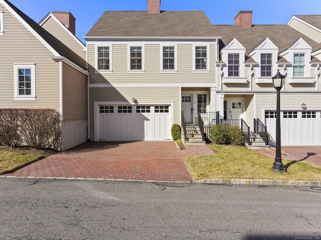 view of front facade with driveway, an attached garage, a chimney, and a front lawn