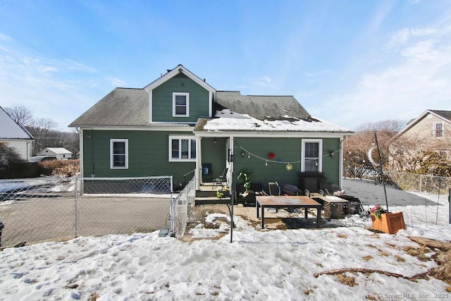 snow covered house featuring fence and roof with shingles