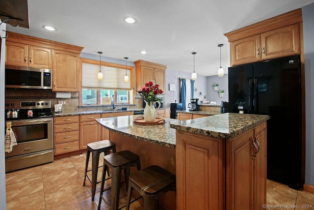 kitchen featuring stone counters, stainless steel appliances, a sink, a kitchen island, and hanging light fixtures