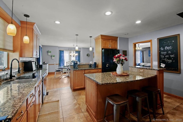 kitchen with hanging light fixtures, freestanding refrigerator, a kitchen island, a sink, and dark stone countertops