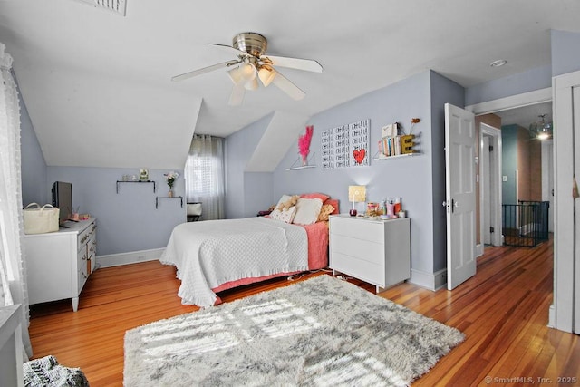 bedroom featuring light wood-type flooring, vaulted ceiling, baseboards, and ceiling fan