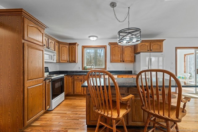 kitchen with a wealth of natural light, white appliances, light wood-style floors, and brown cabinetry