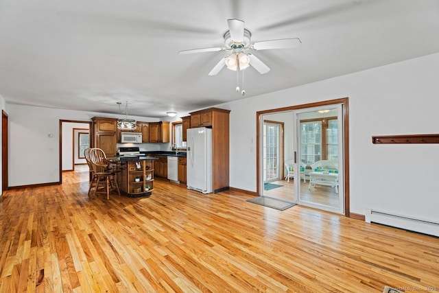 kitchen featuring dark countertops, light wood finished floors, a baseboard heating unit, a breakfast bar, and white appliances