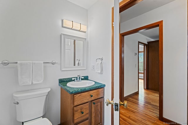 bathroom featuring baseboards, toilet, wood finished floors, and vanity