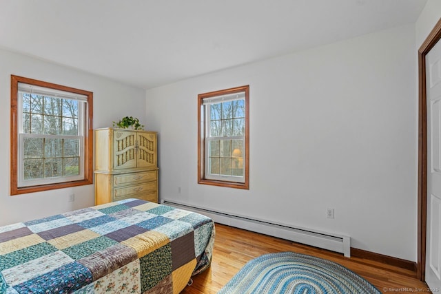 bedroom featuring a baseboard heating unit, multiple windows, and wood finished floors