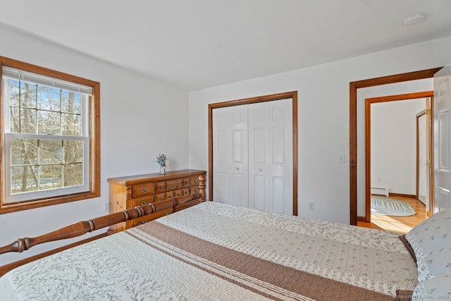 bedroom with wood finished floors, a closet, and a baseboard radiator