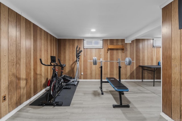 workout room featuring light wood finished floors, baseboards, and wood walls