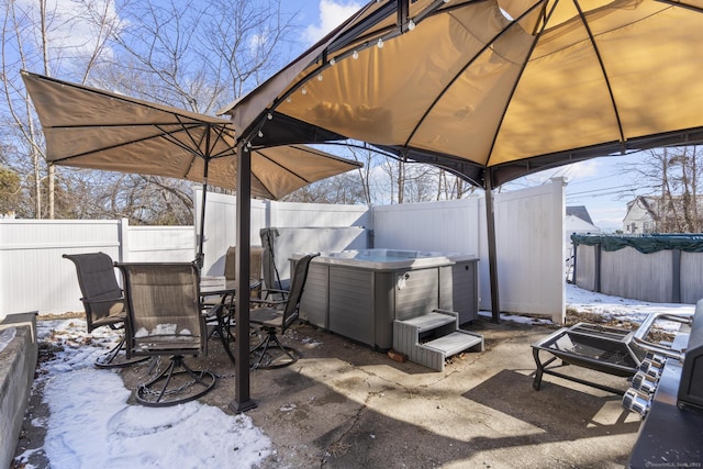 snow covered patio with a fenced backyard, a hot tub, and a gazebo