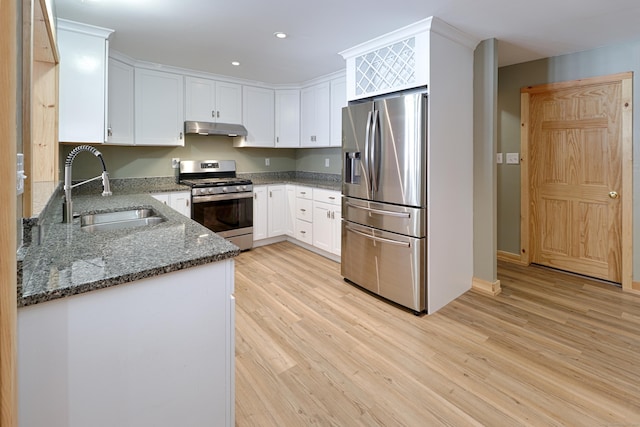 kitchen with under cabinet range hood, a sink, white cabinets, appliances with stainless steel finishes, and dark stone countertops