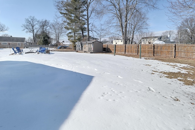 snowy yard featuring a storage shed, a fenced backyard, and an outdoor structure