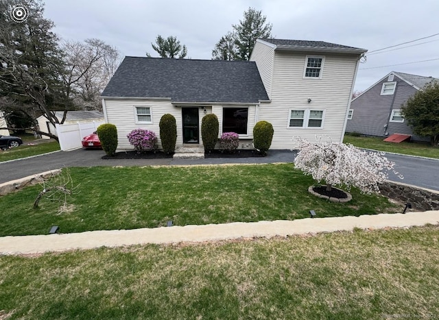 traditional home featuring a shingled roof, a front yard, and fence