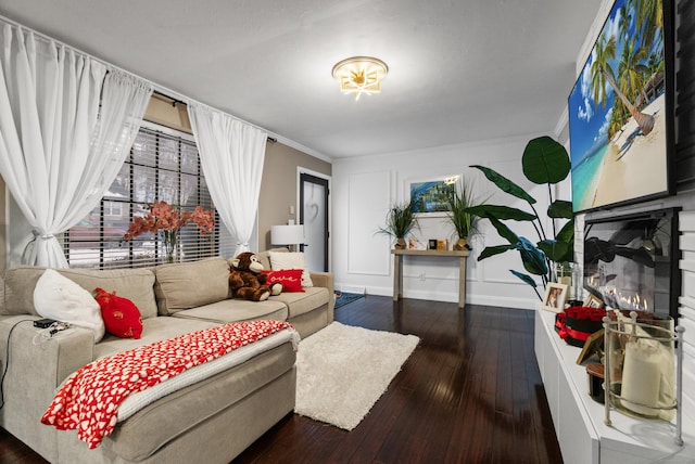 living area with a warm lit fireplace, baseboards, dark wood finished floors, and crown molding