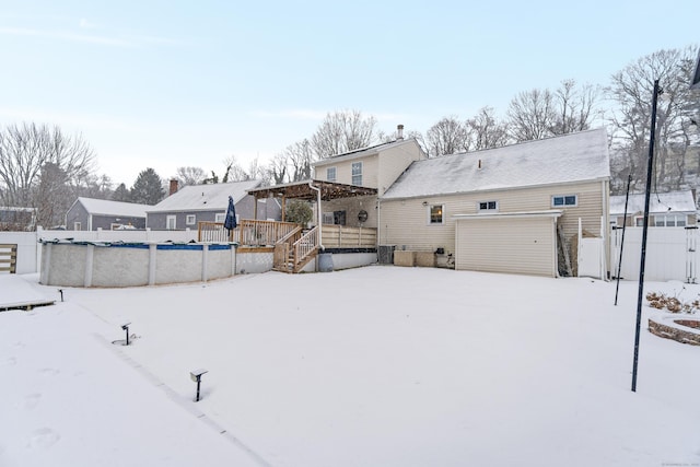 snow covered house featuring an attached garage, fence, and a fenced in pool