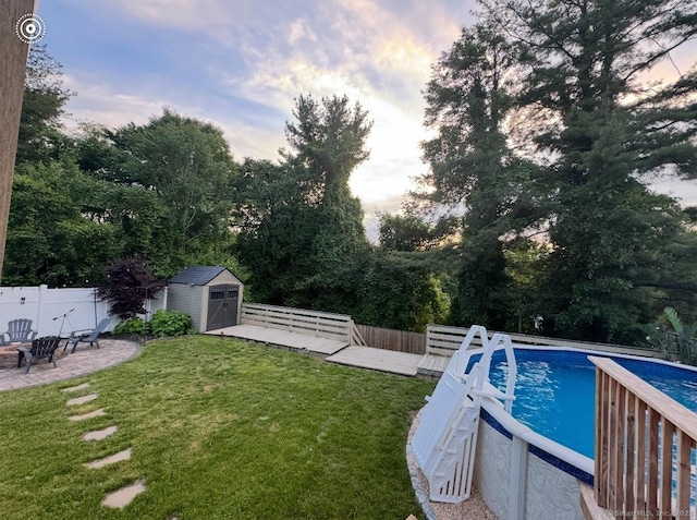 pool at dusk with an outbuilding, a lawn, a shed, a fenced backyard, and an outdoor pool