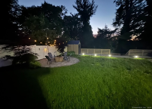 view of yard featuring a fire pit, a storage unit, an outdoor structure, and a fenced backyard