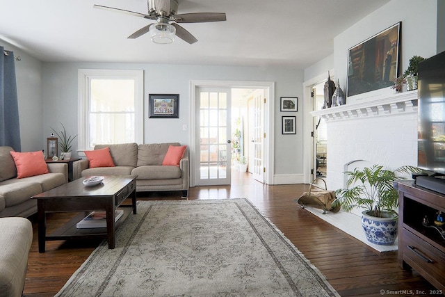 living area with ceiling fan, plenty of natural light, wood finished floors, and a brick fireplace